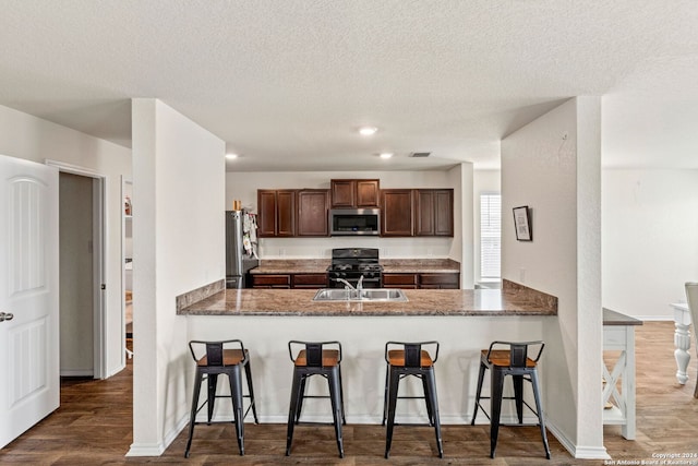 kitchen with a kitchen breakfast bar, hardwood / wood-style flooring, stainless steel appliances, and kitchen peninsula