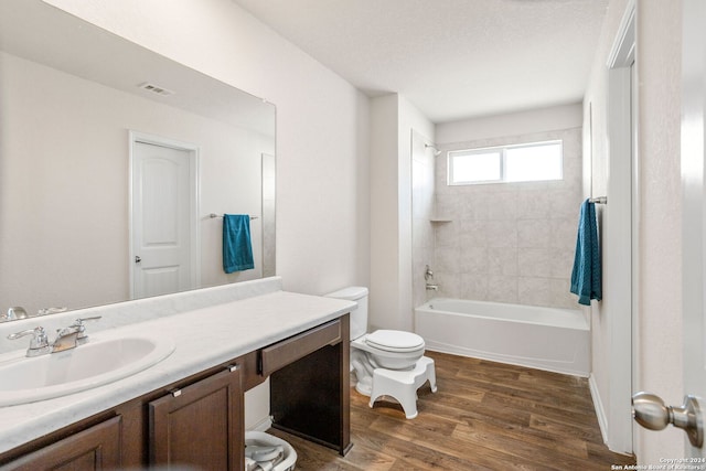 full bathroom featuring a textured ceiling, vanity, toilet, tiled shower / bath, and hardwood / wood-style flooring