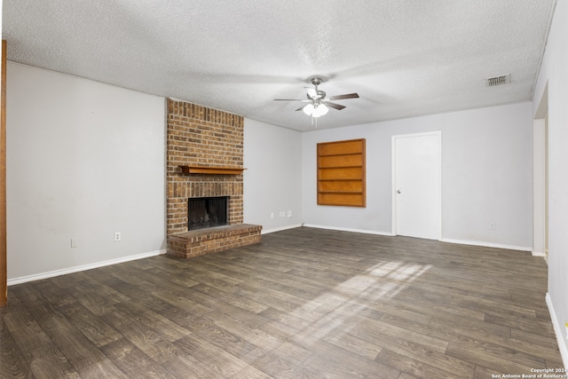 unfurnished living room with a brick fireplace, ceiling fan, dark wood-type flooring, built in shelves, and a textured ceiling