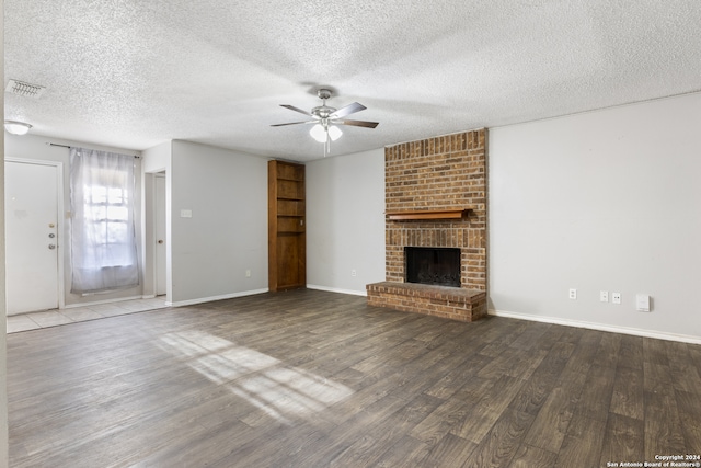 unfurnished living room featuring ceiling fan, hardwood / wood-style flooring, a brick fireplace, and a textured ceiling