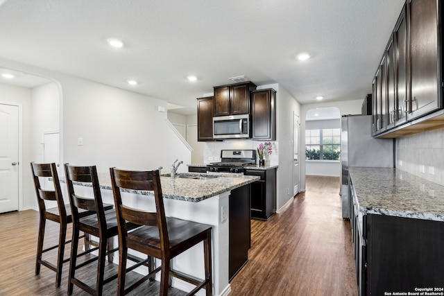 kitchen featuring a center island with sink, dark hardwood / wood-style floors, light stone countertops, appliances with stainless steel finishes, and a kitchen bar