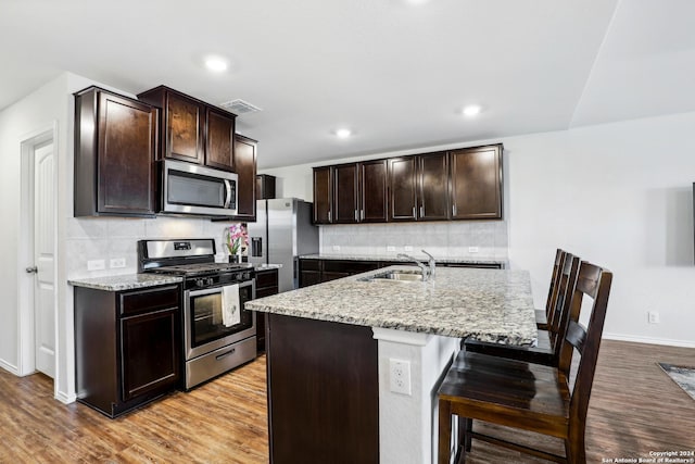 kitchen featuring visible vents, dark brown cabinets, a breakfast bar area, light wood-style flooring, and stainless steel appliances