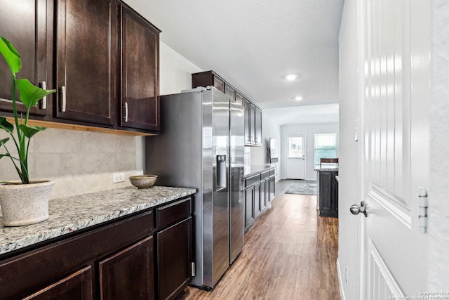 kitchen featuring backsplash, stainless steel refrigerator with ice dispenser, light stone countertops, light wood-type flooring, and dark brown cabinetry