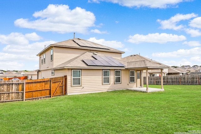 rear view of house with solar panels, a patio area, and a yard