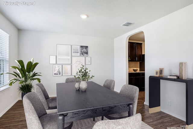 dining space featuring visible vents, arched walkways, baseboards, and dark wood finished floors