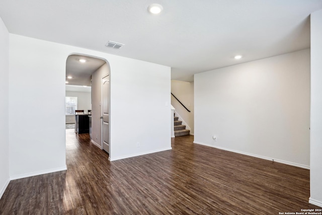 spare room featuring visible vents, baseboards, stairs, arched walkways, and dark wood-style flooring