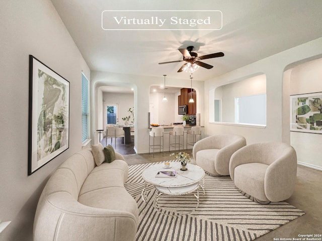 living room featuring baseboards, arched walkways, and ceiling fan