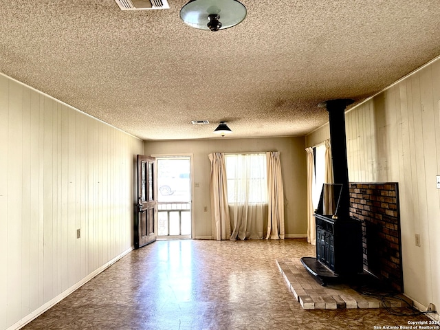 unfurnished living room featuring wooden walls, a wood stove, and a textured ceiling