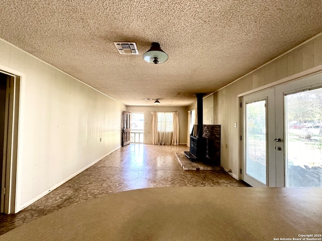 unfurnished living room featuring plenty of natural light, a wood stove, and a textured ceiling