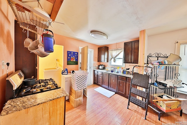 kitchen featuring light stone counters, light wood-style floors, dark brown cabinetry, and gas range oven