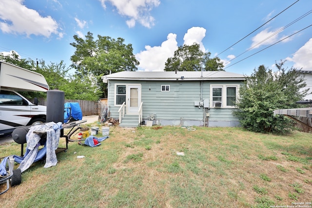 rear view of house with entry steps, a lawn, and fence