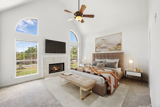 carpeted bedroom featuring ceiling fan, a fireplace, high vaulted ceiling, and multiple windows