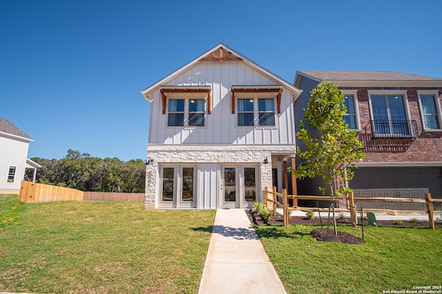 view of front of property with board and batten siding, fence, a front yard, french doors, and stone siding