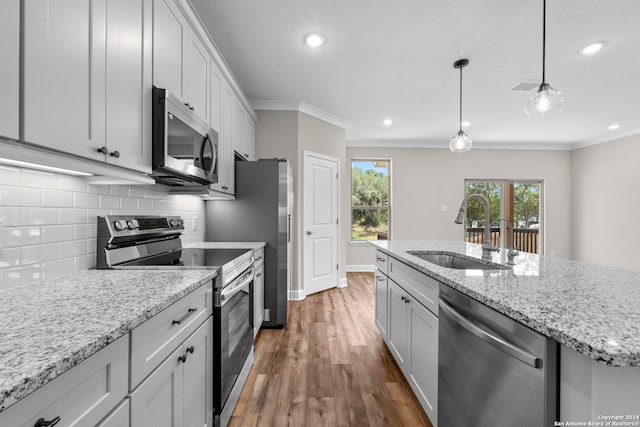 kitchen with crown molding, sink, dark hardwood / wood-style floors, appliances with stainless steel finishes, and a center island with sink