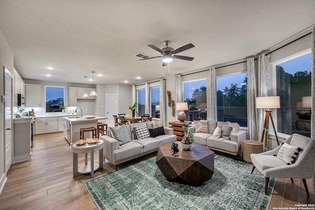 living room featuring a textured ceiling, ceiling fan, sink, and light wood-type flooring