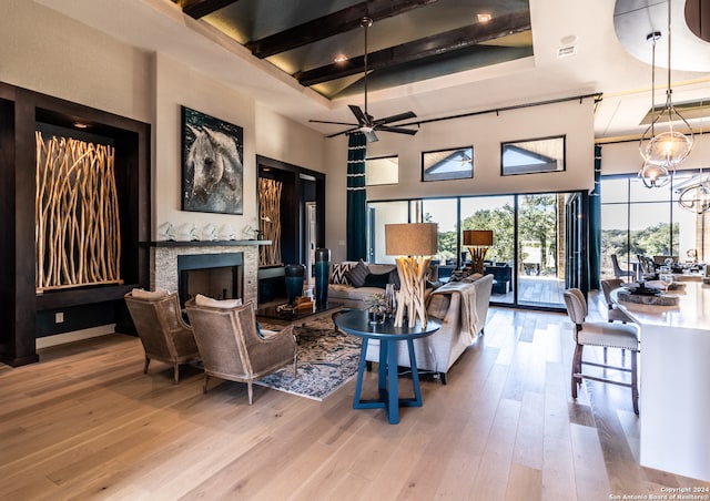 living room featuring a towering ceiling, ceiling fan with notable chandelier, beam ceiling, a fireplace, and light hardwood / wood-style floors