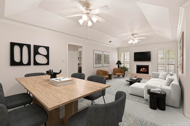 carpeted dining room with a raised ceiling, ceiling fan, and a brick fireplace