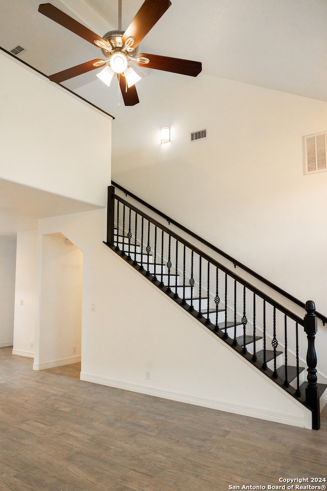 staircase featuring high vaulted ceiling, ceiling fan, and wood-type flooring