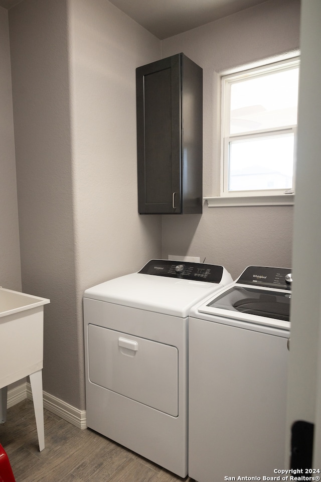 laundry area featuring hardwood / wood-style flooring, washing machine and dryer, and cabinets