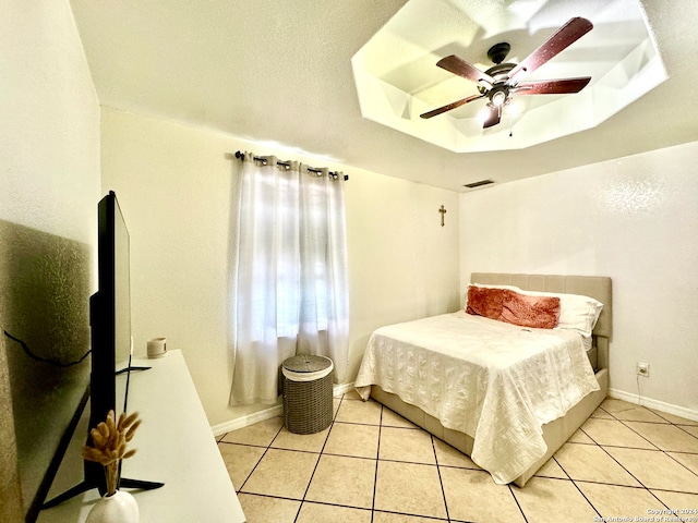 tiled bedroom featuring a tray ceiling, a textured ceiling, and ceiling fan