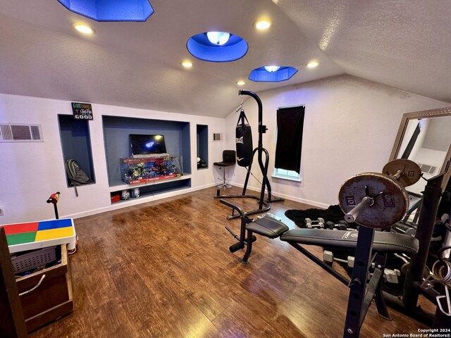 exercise room with a textured ceiling, hardwood / wood-style flooring, and lofted ceiling