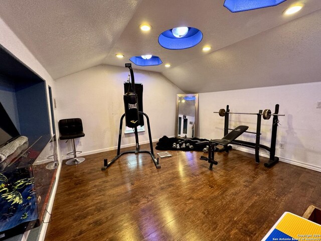 workout area featuring dark wood-type flooring, vaulted ceiling, and a textured ceiling