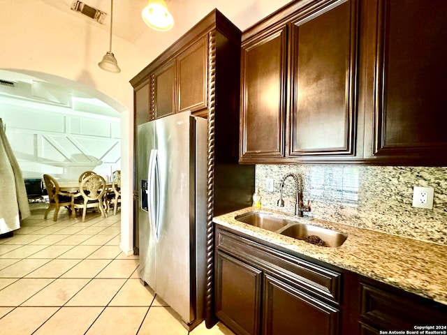 kitchen featuring light stone countertops, stainless steel fridge, decorative light fixtures, light tile patterned floors, and sink