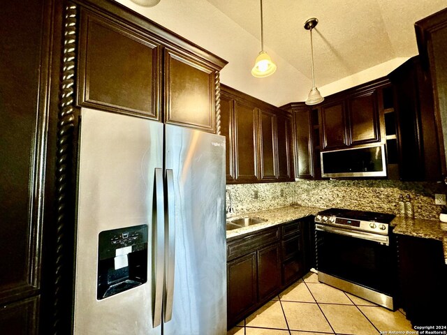 kitchen with lofted ceiling, light stone counters, decorative light fixtures, and appliances with stainless steel finishes