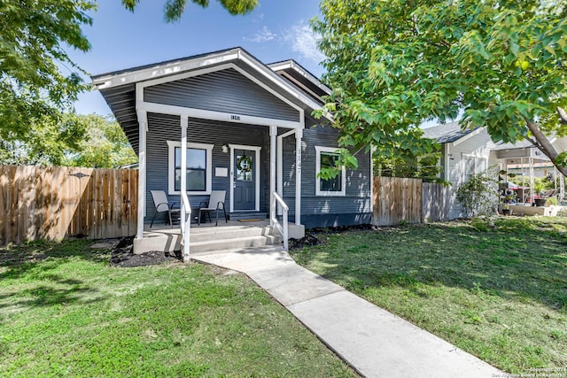 view of front of house with covered porch, a front lawn, and fence