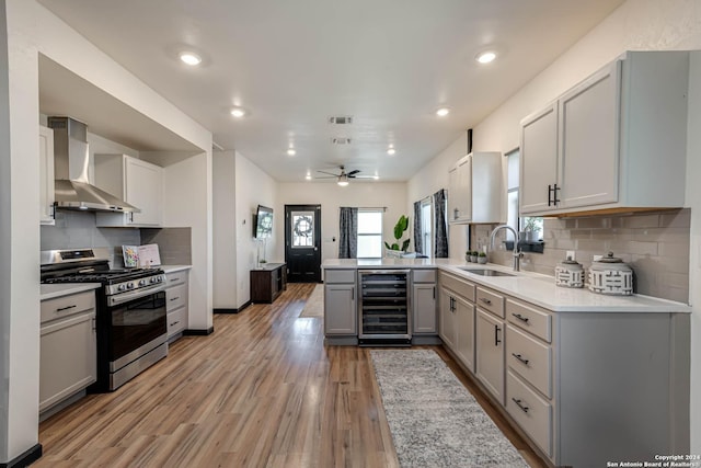 kitchen with beverage cooler, gray cabinets, a sink, gas range, and wall chimney exhaust hood