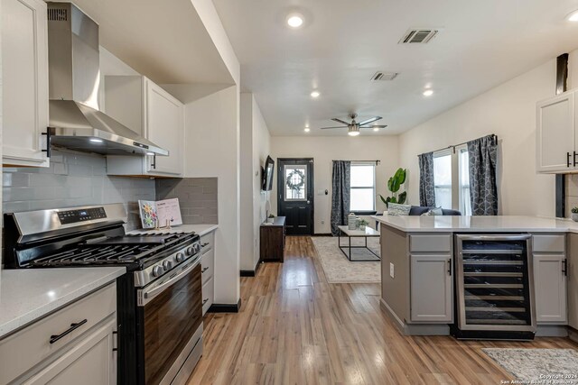 kitchen featuring wall chimney range hood, white cabinets, stainless steel appliances, and light hardwood / wood-style floors