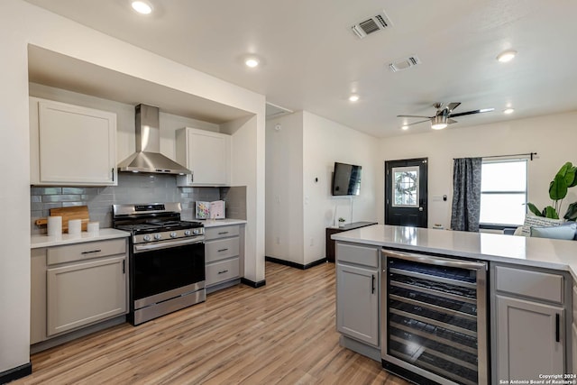 kitchen featuring beverage cooler, gray cabinets, wall chimney exhaust hood, and stainless steel gas stove