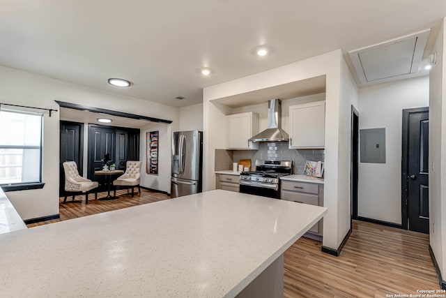 kitchen with light wood-type flooring, white cabinetry, tasteful backsplash, wall chimney exhaust hood, and appliances with stainless steel finishes