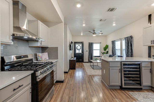 kitchen with gas range, light hardwood / wood-style floors, wall chimney range hood, wine cooler, and decorative backsplash