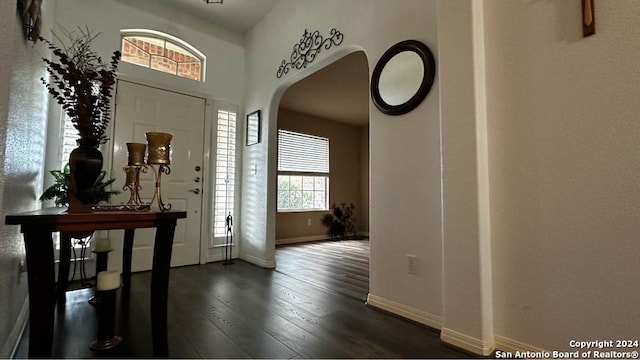 foyer with baseboards, arched walkways, and dark wood-type flooring