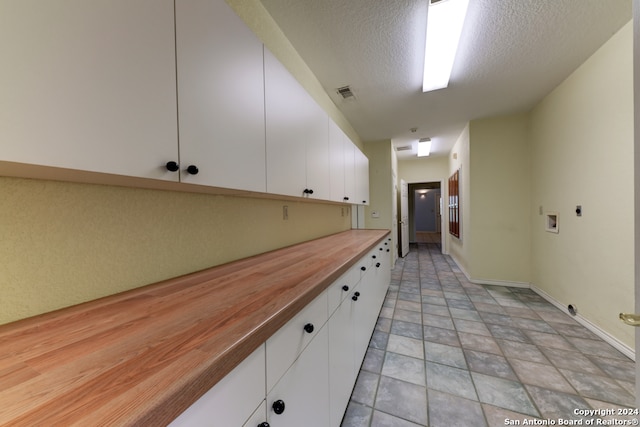 kitchen featuring a textured ceiling, butcher block countertops, and white cabinetry