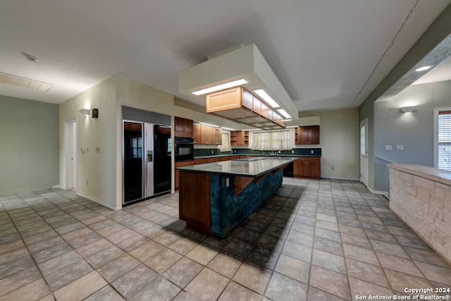 kitchen featuring a skylight, light tile patterned floors, black appliances, a center island, and a breakfast bar area