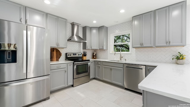 kitchen with light stone counters, stainless steel appliances, sink, gray cabinets, and wall chimney exhaust hood