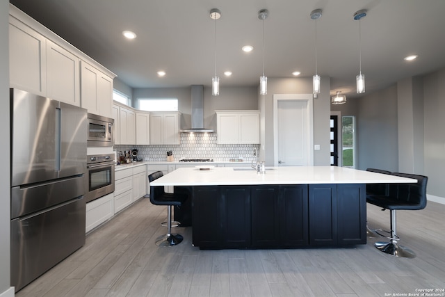 kitchen with light hardwood / wood-style floors, appliances with stainless steel finishes, wall chimney exhaust hood, and a healthy amount of sunlight