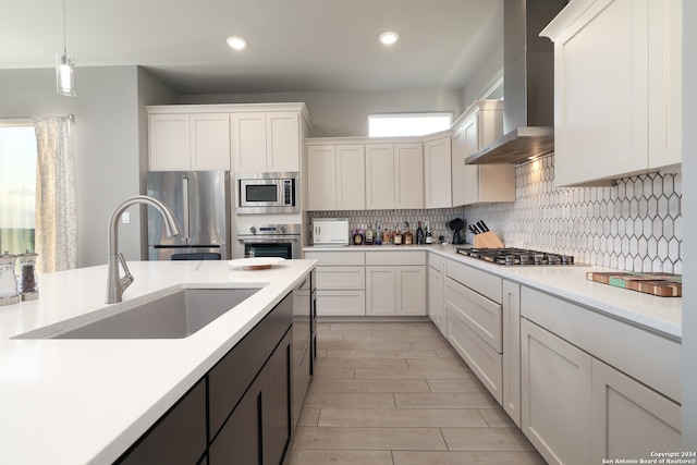 kitchen with sink, wall chimney range hood, appliances with stainless steel finishes, and white cabinetry