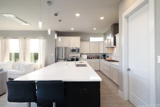 kitchen featuring light wood-type flooring, stainless steel appliances, white cabinetry, wall chimney range hood, and a kitchen island with sink