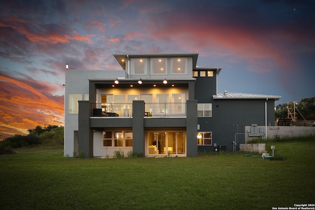 back house at dusk with a balcony and a lawn