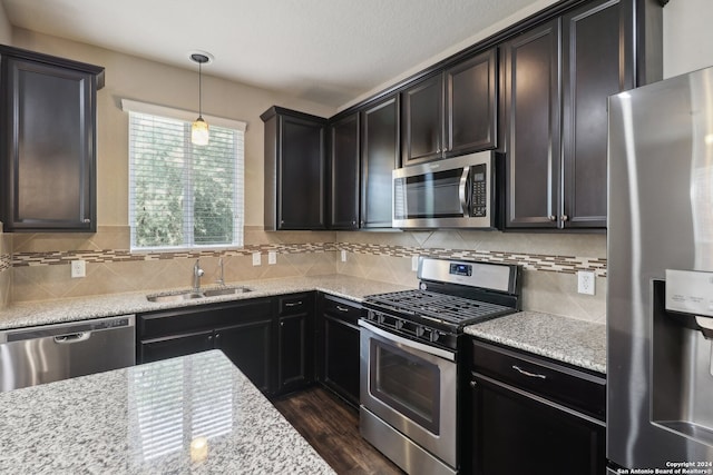 kitchen with pendant lighting, stainless steel appliances, dark hardwood / wood-style flooring, sink, and light stone countertops