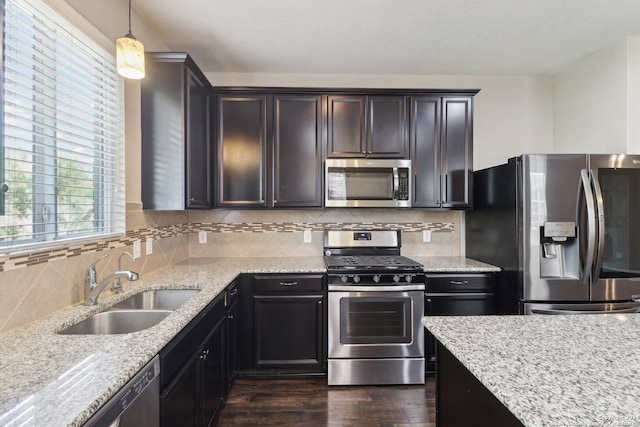 kitchen with pendant lighting, sink, light stone countertops, dark wood-type flooring, and appliances with stainless steel finishes