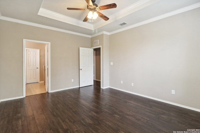 unfurnished bedroom with a tray ceiling, dark wood-type flooring, crown molding, and ceiling fan