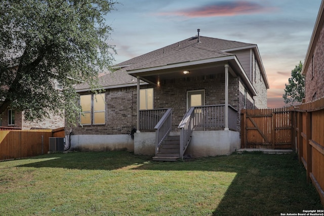 back house at dusk featuring a lawn and central air condition unit