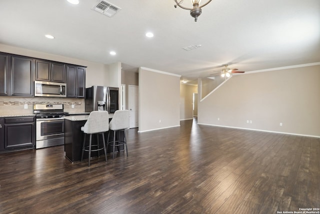 kitchen featuring appliances with stainless steel finishes, crown molding, a center island, dark wood-type flooring, and ceiling fan