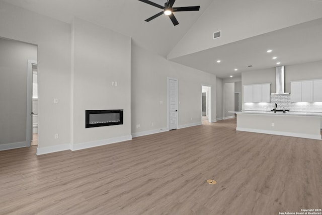 unfurnished living room with ceiling fan, high vaulted ceiling, sink, and light hardwood / wood-style floors