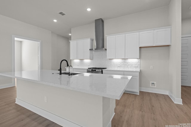 kitchen featuring wall chimney exhaust hood, sink, a kitchen island with sink, and white cabinets