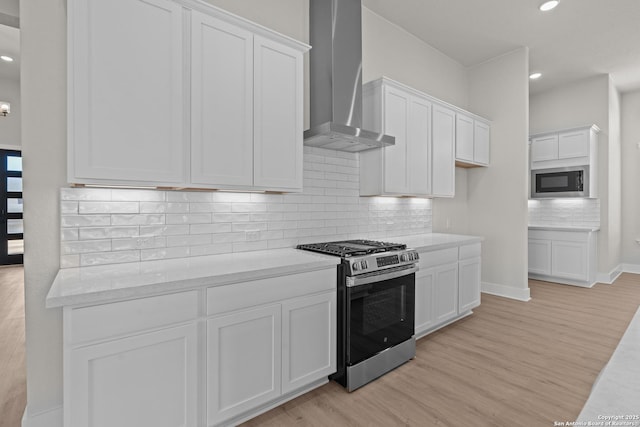 kitchen featuring built in microwave, gas range, wall chimney range hood, light hardwood / wood-style floors, and white cabinets